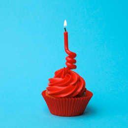 Photo of Delicious birthday cupcake with red cream and burning candle on light blue background