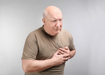 Senior man suffering from pain in chest on light background