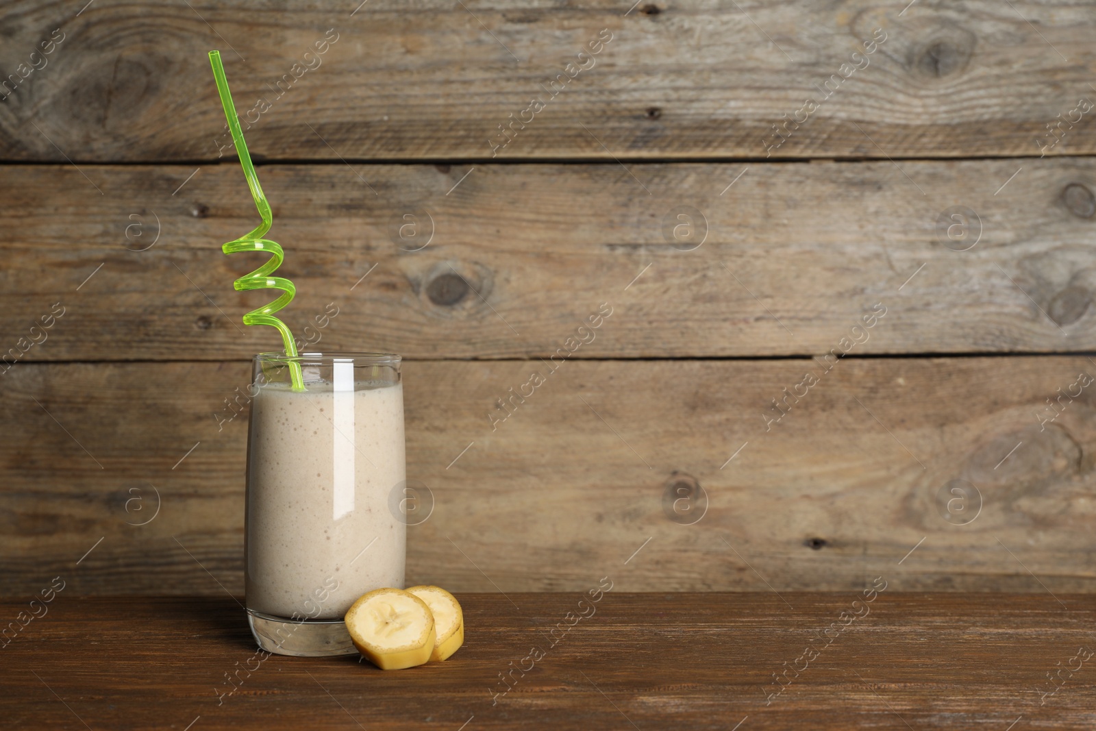 Photo of Glass of tasty smoothie with straw and cut banana on wooden table. Space for text