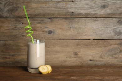 Glass of tasty smoothie with straw and cut banana on wooden table. Space for text