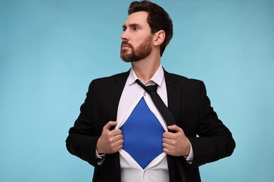 Photo of Confident businessman wearing superhero costume under suit on light blue background