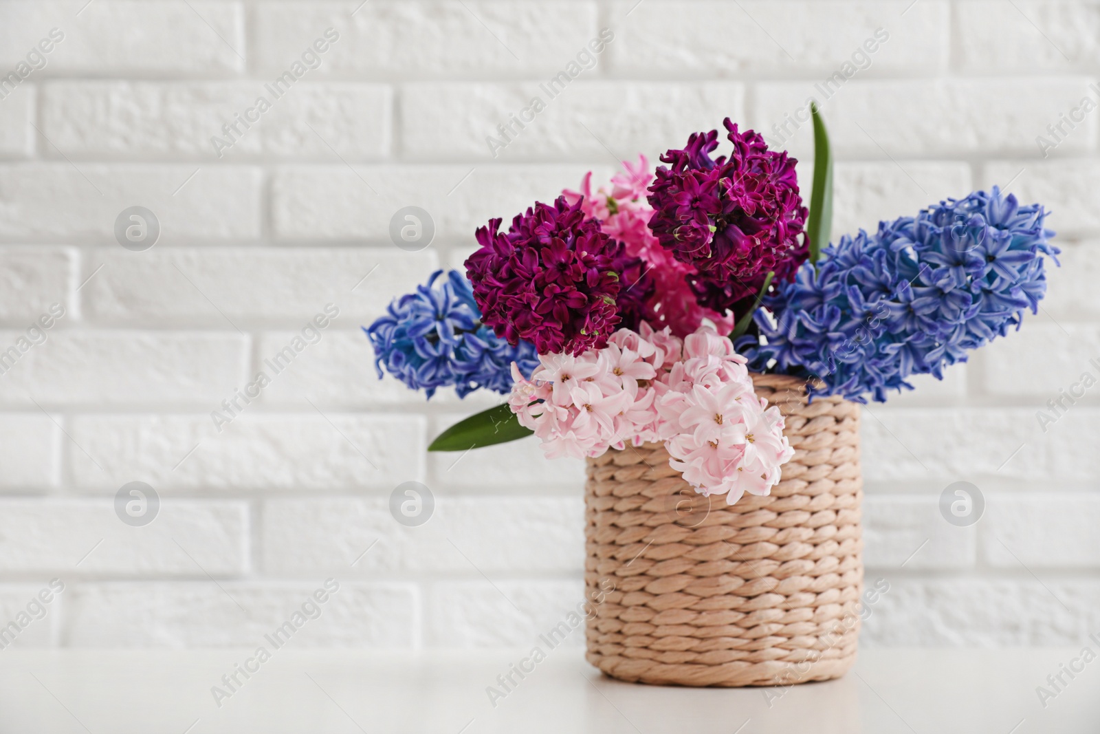 Photo of Beautiful hyacinths in wicker pot on table against brick wall, space for text. Spring flowers