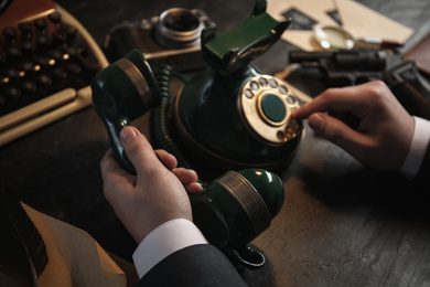 Photo of Detective dialing number on vintage telephone at table, closeup