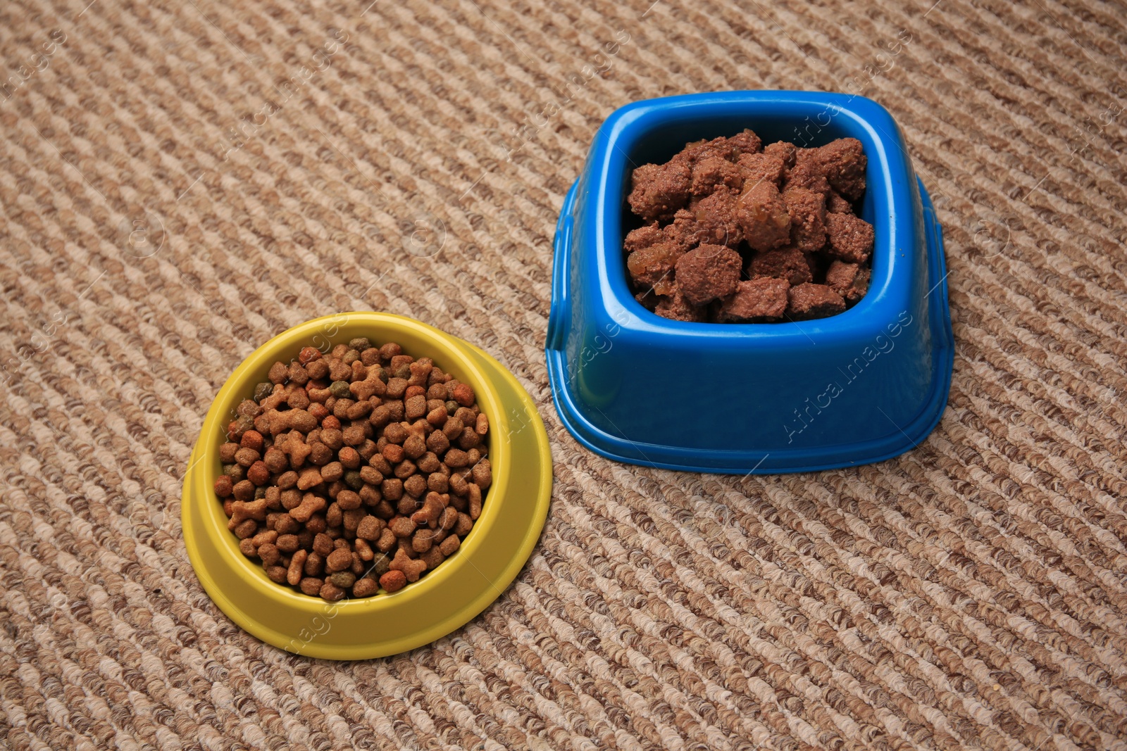 Photo of Dry and wet pet food in feeding bowls on soft carpet, above view