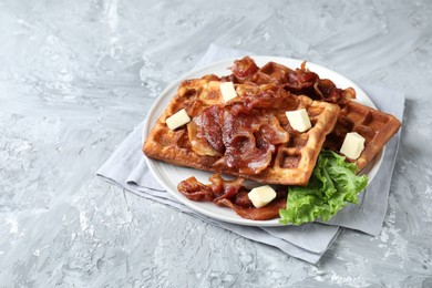 Photo of Delicious Belgium waffles served with fried bacon and butter on grey table, space for text