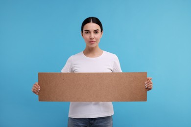 Woman holding blank cardboard banner on light blue background, space for text