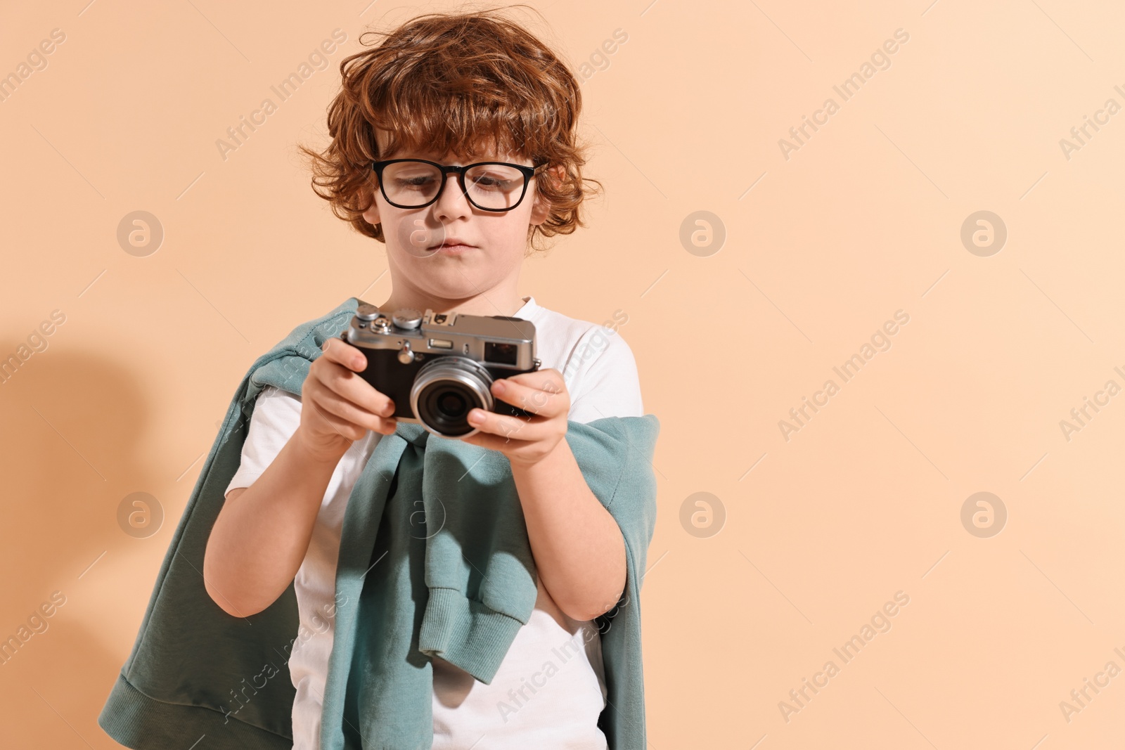 Photo of Fashion concept. Stylish boy with vintage camera on pale orange background. Space for text