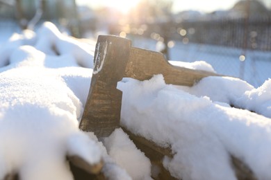 Metal axe on snowy firewood outdoors on sunny winter day, closeup