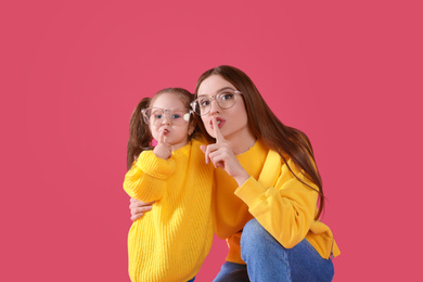 Photo of Young mother and little daughter with glasses on pink background