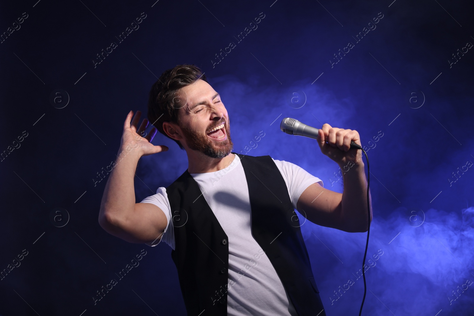 Photo of Handsome man with microphone singing on dark blue background