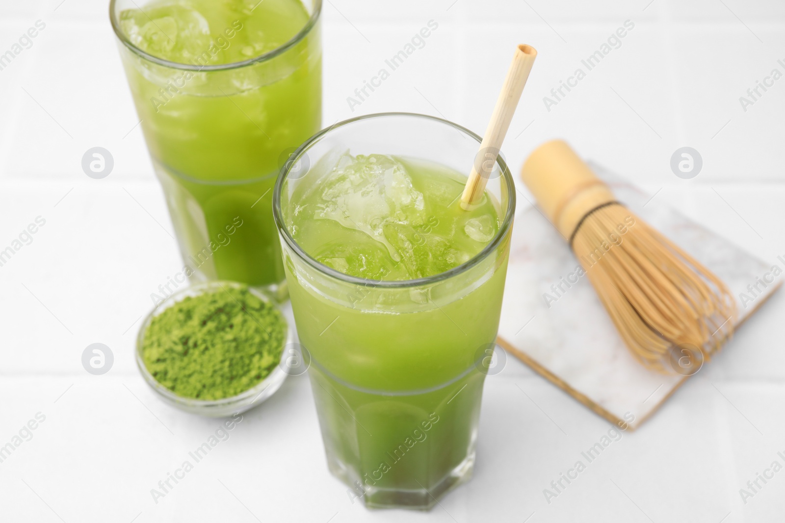 Photo of Delicious iced green matcha tea, powder and bamboo whisk on white table