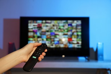 Photo of Woman switching channels on TV set with remote control at home, closeup. Space for text