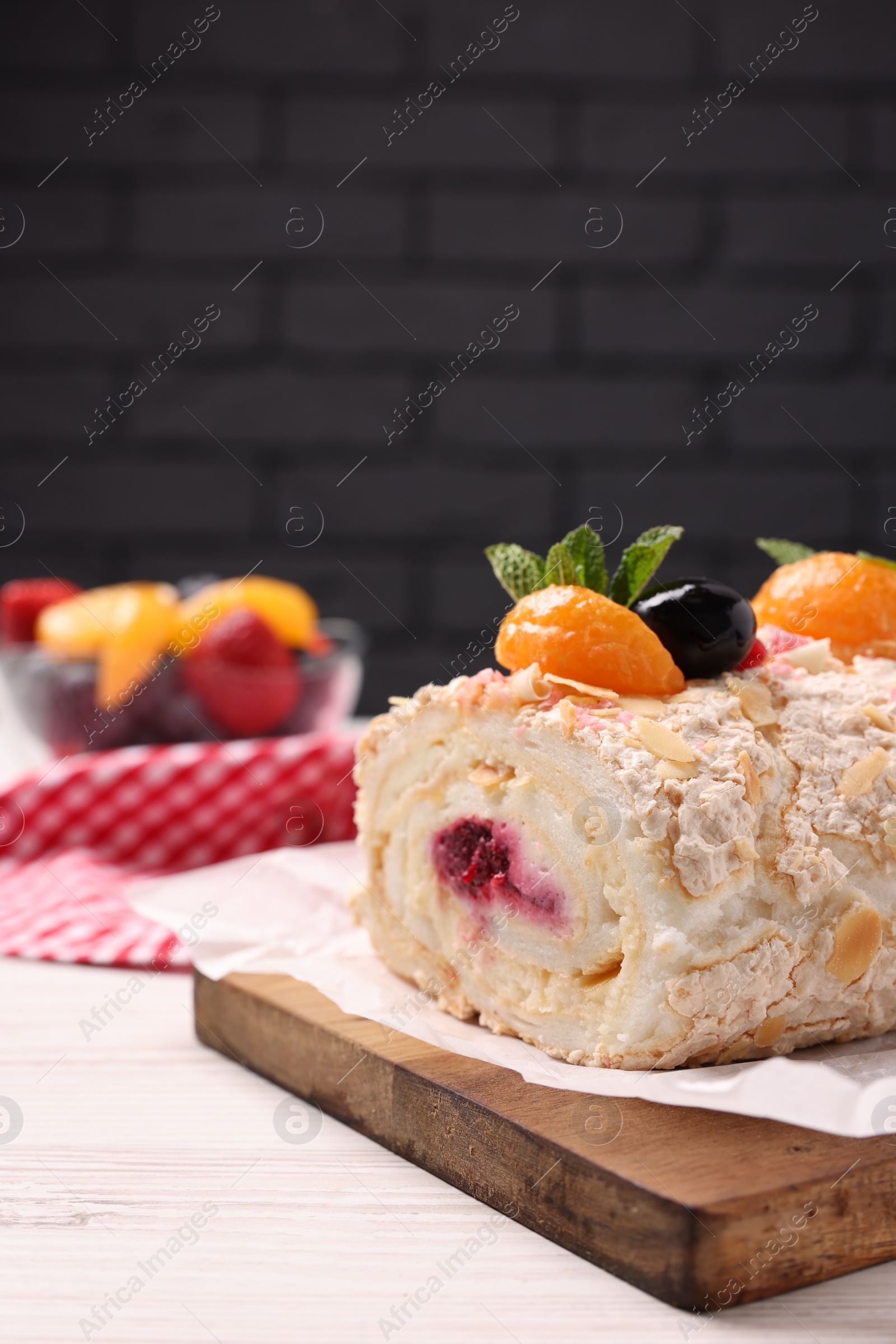 Photo of Tasty meringue roll with jam, tangerine slices and mint leaves on white wooden table, closeup