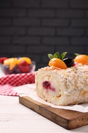 Tasty meringue roll with jam, tangerine slices and mint leaves on white wooden table, closeup