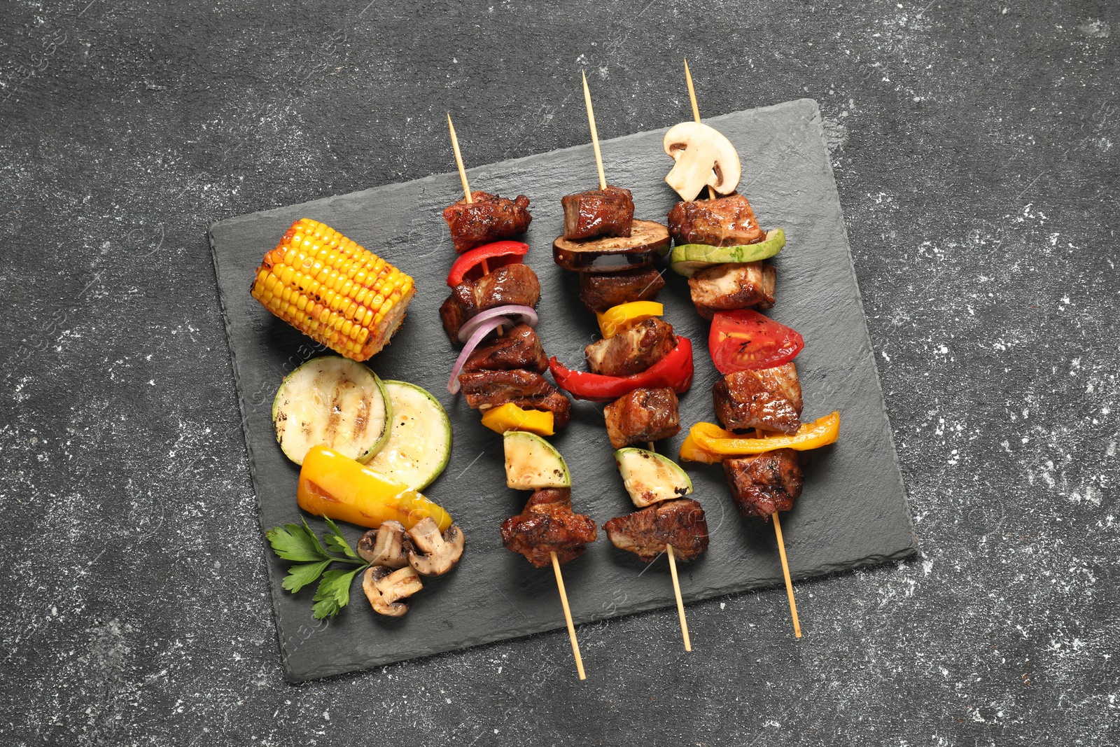Photo of Delicious shish kebabs with grilled vegetables on grey textured table, top view