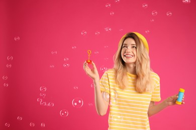 Young woman blowing soap bubbles on pink background, space for text