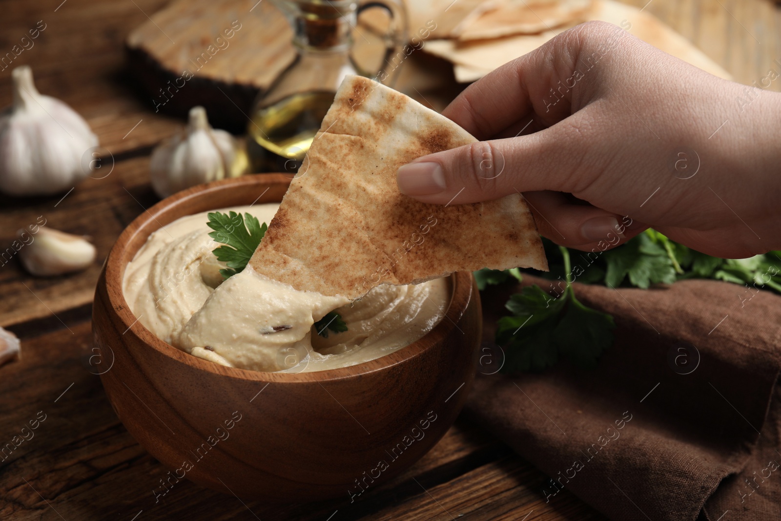 Photo of Woman dipping pita chip into hummus at wooden table, closeup