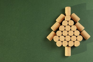 Photo of Christmas tree made of wine corks on green background, top view. Space for text