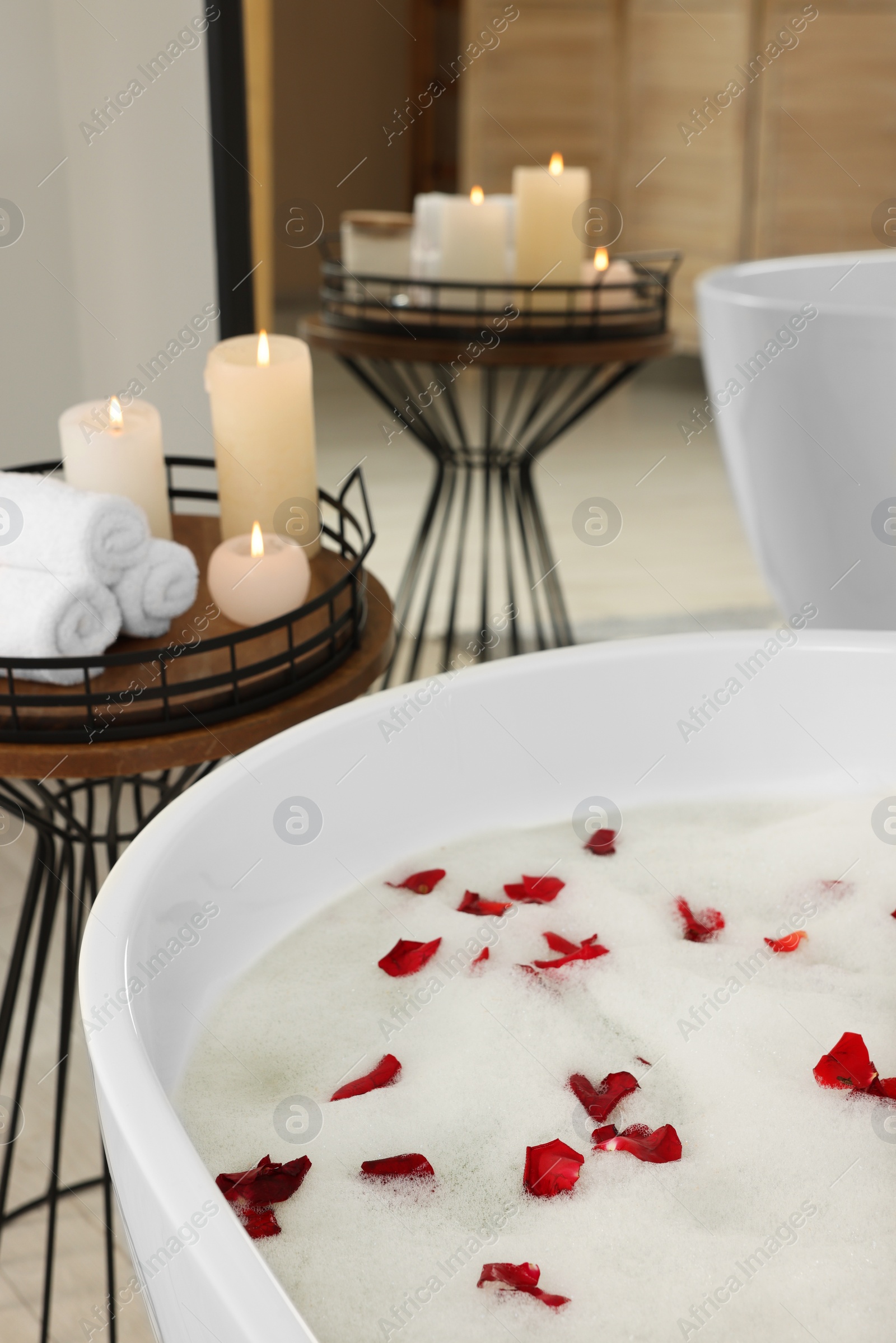 Photo of Bath tub with foam and rose petals in bathroom