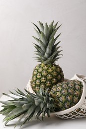 Net bag with delicious ripe pineapples on white table near light grey wall