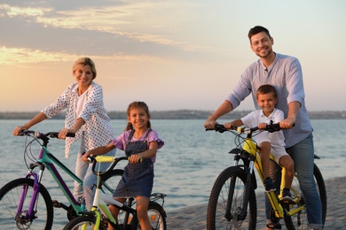 Photo of Happy family with children riding bicycles near river at sunset