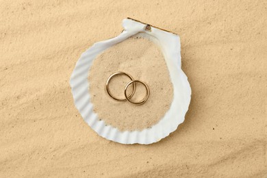 Photo of Honeymoon concept. Two golden rings and shell on sand