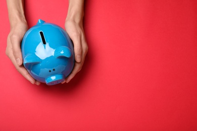 Woman holding piggy bank on red background, top view with space for text. Money savings