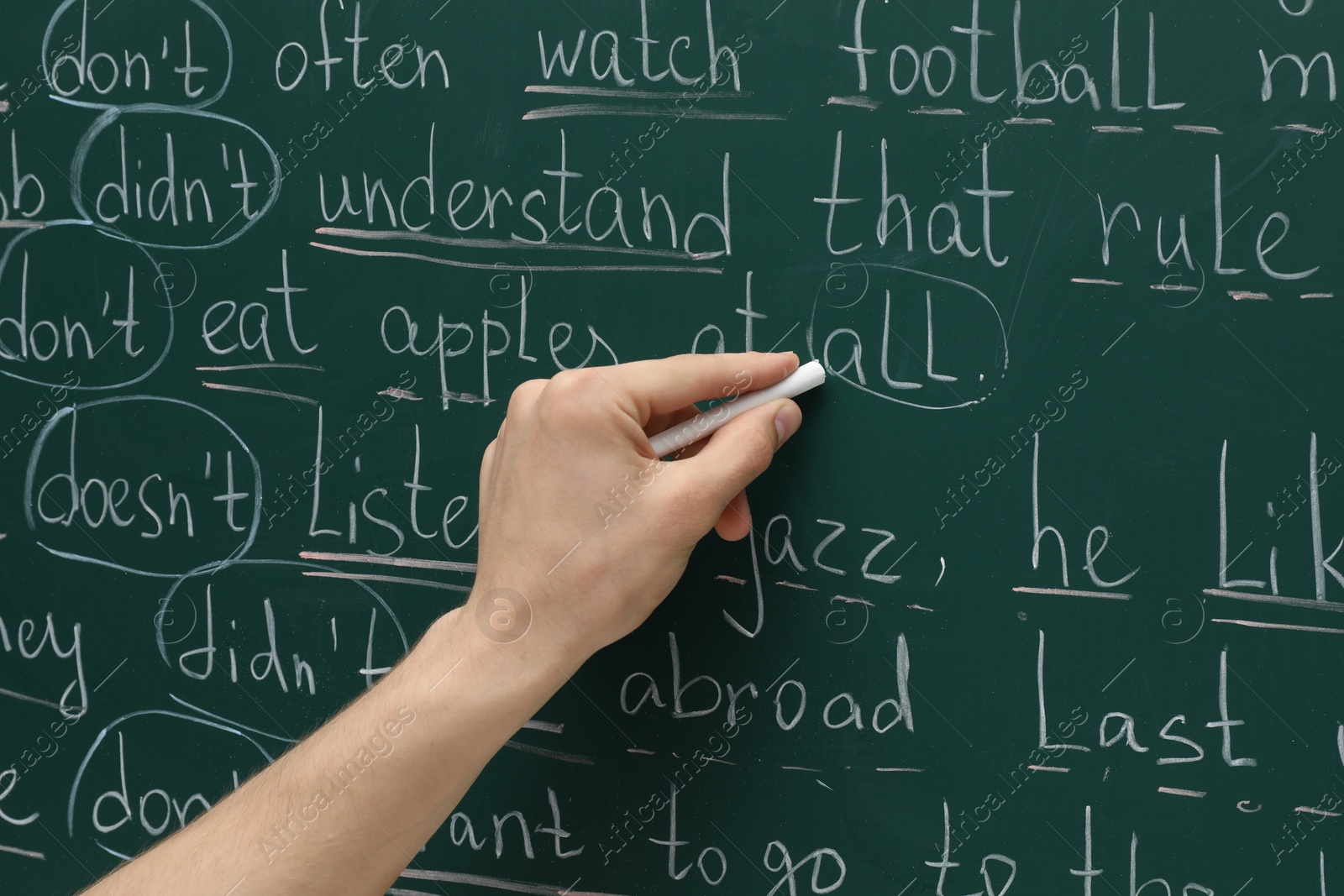 Photo of English teacher writing with chalk on green chalkboard, closeup