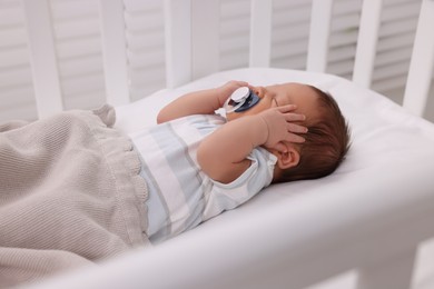 Photo of Cute newborn baby with pacifier sleeping under blanket in crib. Bedtime