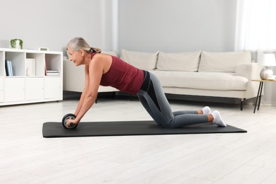 Senior woman in sportswear exercising with abdominal wheel at home. Sports equipment