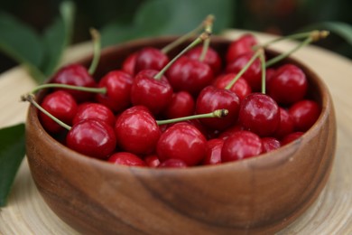 Photo of Tasty ripe red cherries in wooden bowl outdoors, closeup