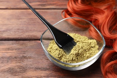 Bowl of henna powder, brush and red strand on wooden table, space for text. Natural hair coloring