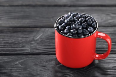 Red mug of tasty fresh bilberries on black wooden table, closeup. Space for text