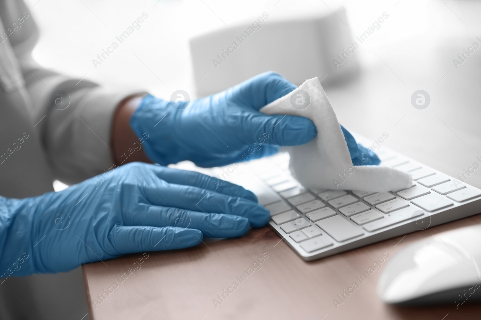 Photo of Woman in latex gloves cleaning computer keyboard with wet wipe at table, closeup