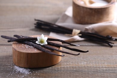 Photo of Vanilla pods, flower and sugar in bowl on wooden table, closeup