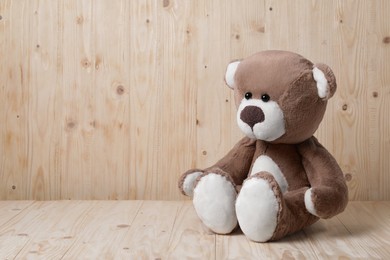 Photo of Cute teddy bear on table near wooden wall, space for text