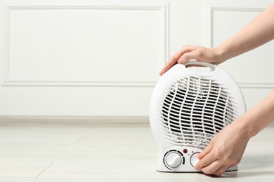 Photo of Young woman adjusting temperature on modern electric fan heater indoors, closeup. Space for text
