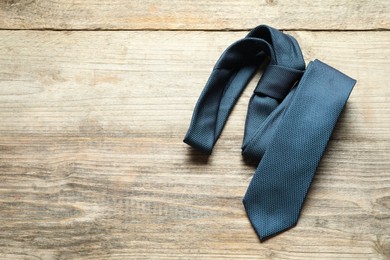 One blue necktie on light wooden table, top view. Space for text