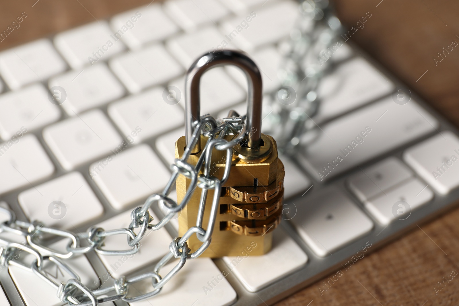 Photo of Cyber security. Keyboard with padlock and chain on wooden table, closeup