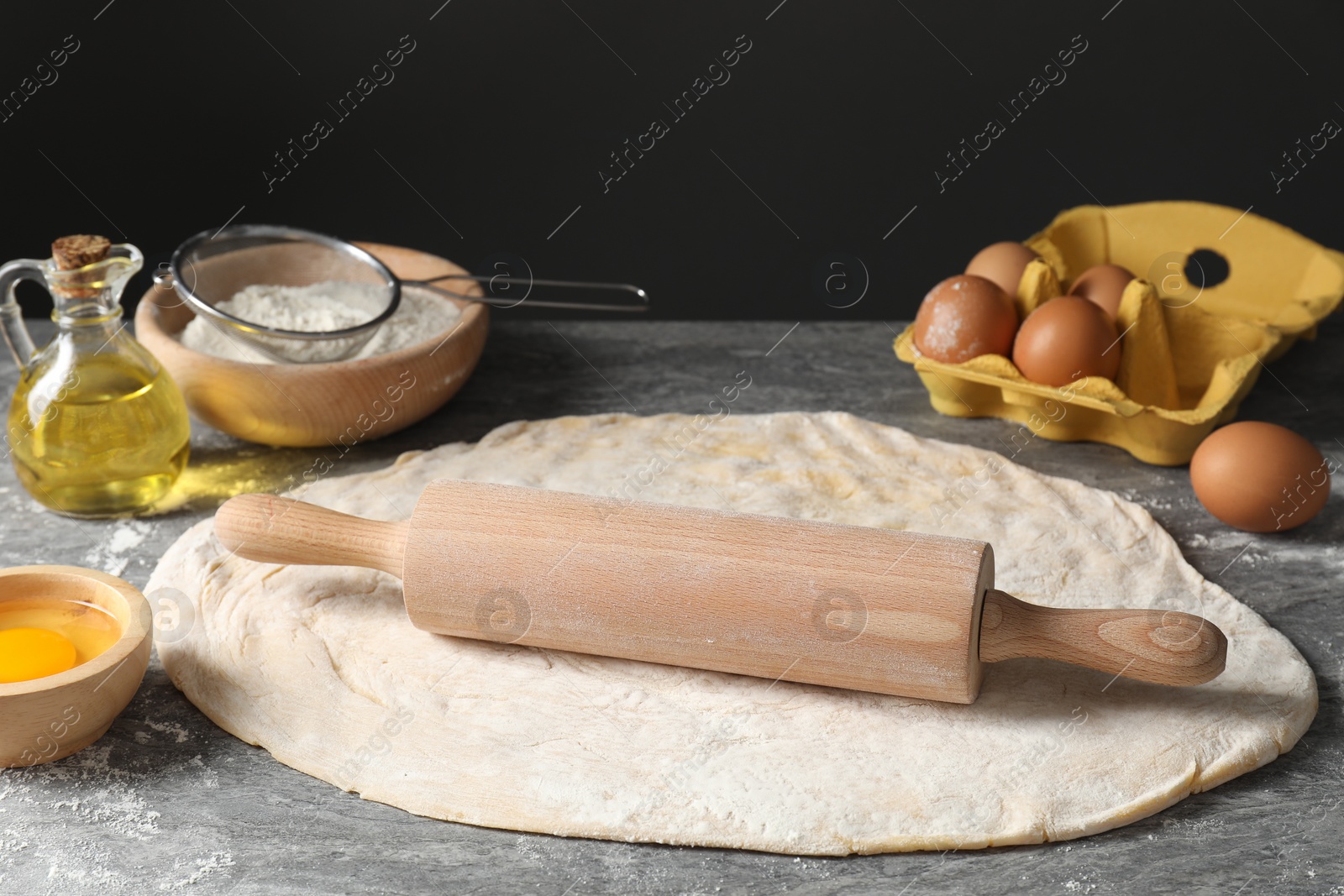 Photo of Raw dough, rolling pin and ingredients on grey table