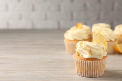 Photo of Tasty cupcake with cream, zest and lemon slice on light wooden table. Space for text