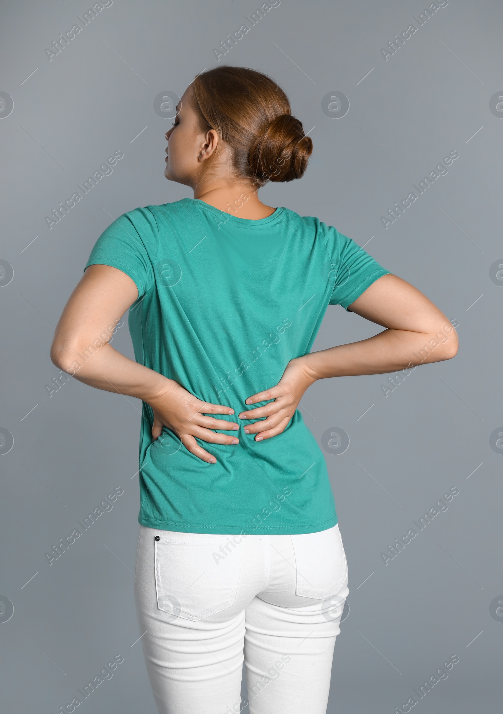 Photo of Woman suffering from back pain on grey background
