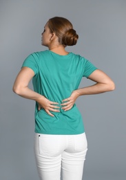 Woman suffering from back pain on grey background