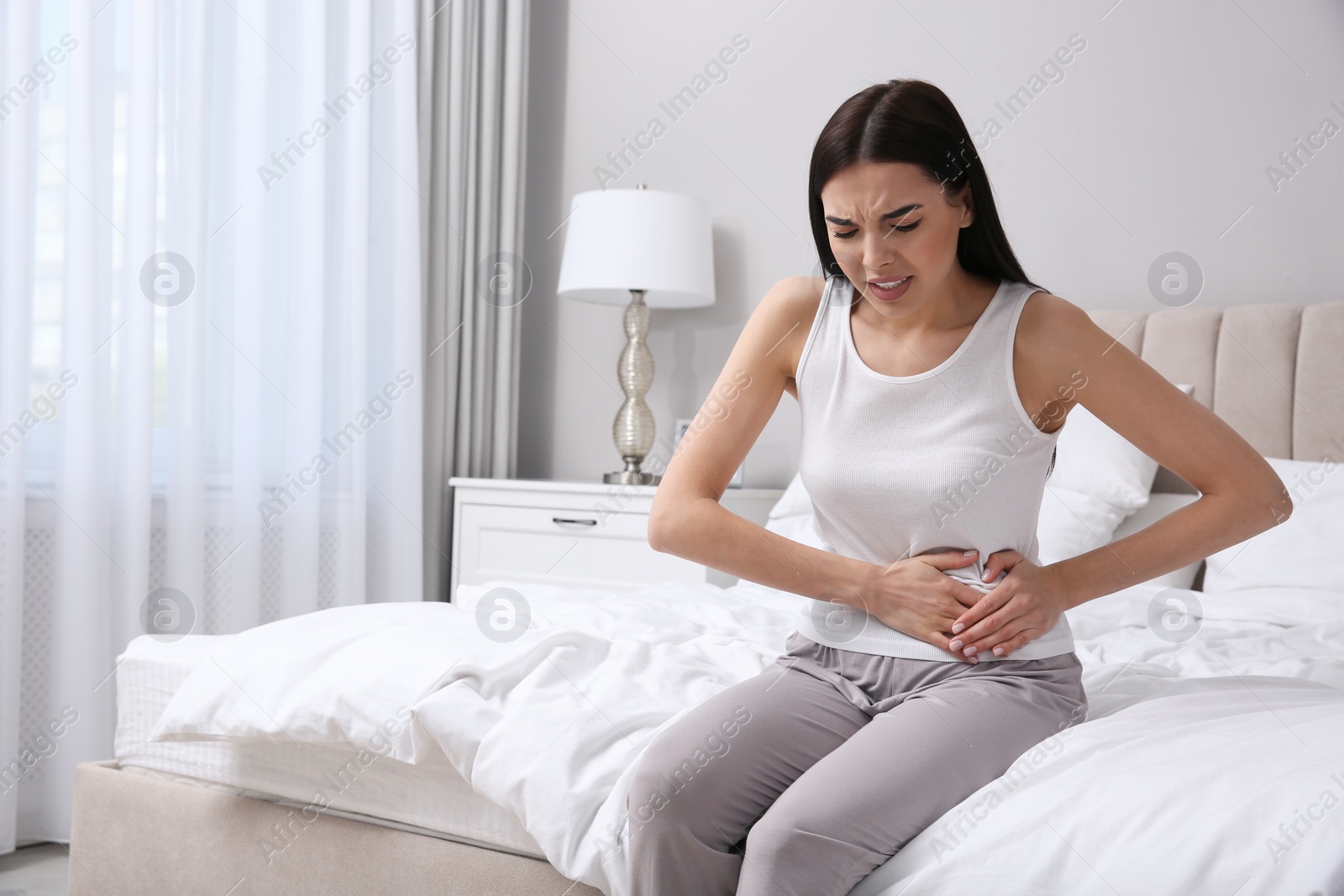 Photo of Young woman suffering from stomach ache in bedroom