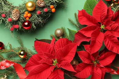 Photo of Flat lay composition with poinsettias (traditional Christmas flowers) and holiday decor on green background