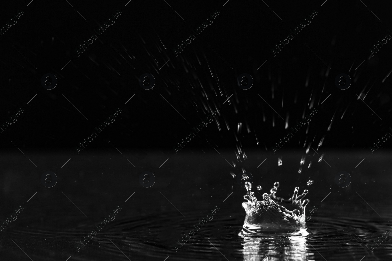 Photo of Rain drop falling down into puddle on dark background, space for text