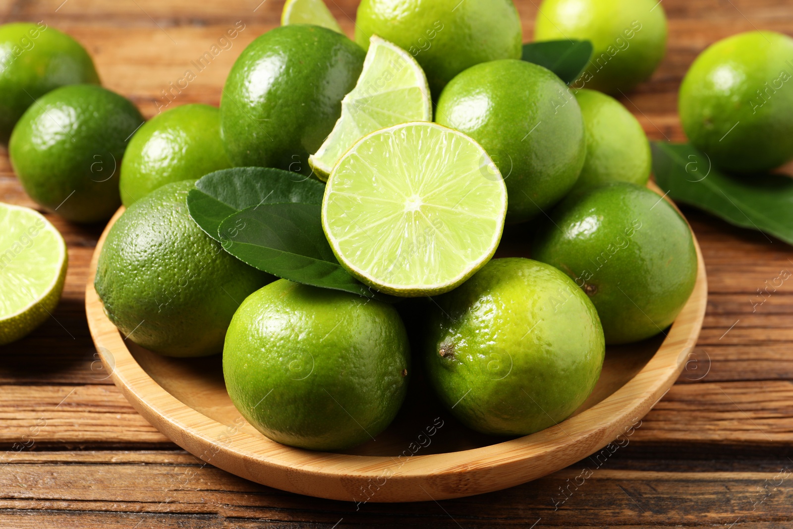 Photo of Fresh ripe limes and green leaves on wooden table, closeup