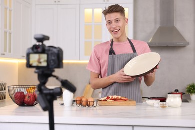 Photo of Smiling food blogger explaining something while recording video in kitchen