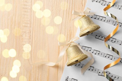 Photo of Golden shiny bells with white bows and music sheet on wooden table, top view and space for text. Christmas decoration