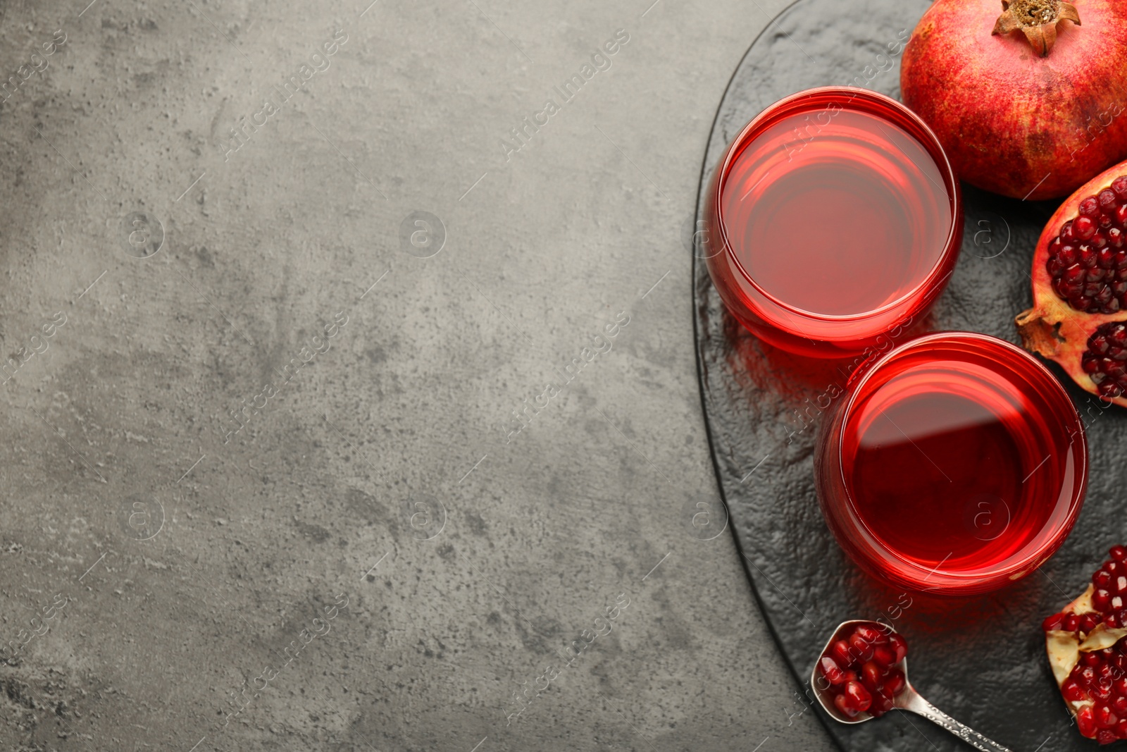 Photo of Tasty pomegranate juice in glasses and fresh fruit on grey table, top view. Space for text